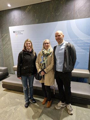 3 Personen, im Hintergrund das Logo des BMBF