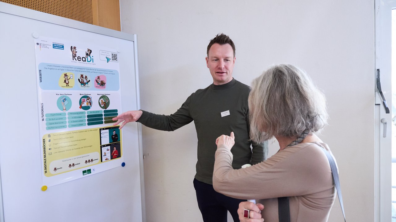 Zwei Personen vor einem Plakat. 